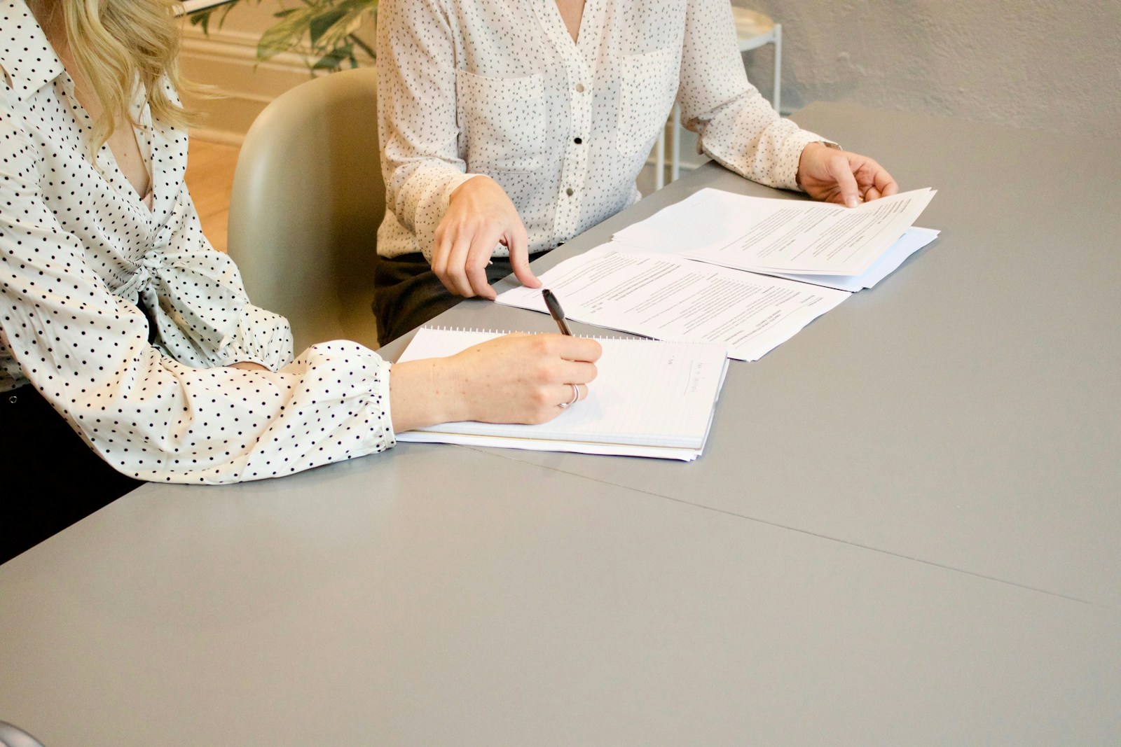 woman signing on white printer paper beside woman about to touch the documents, insurance